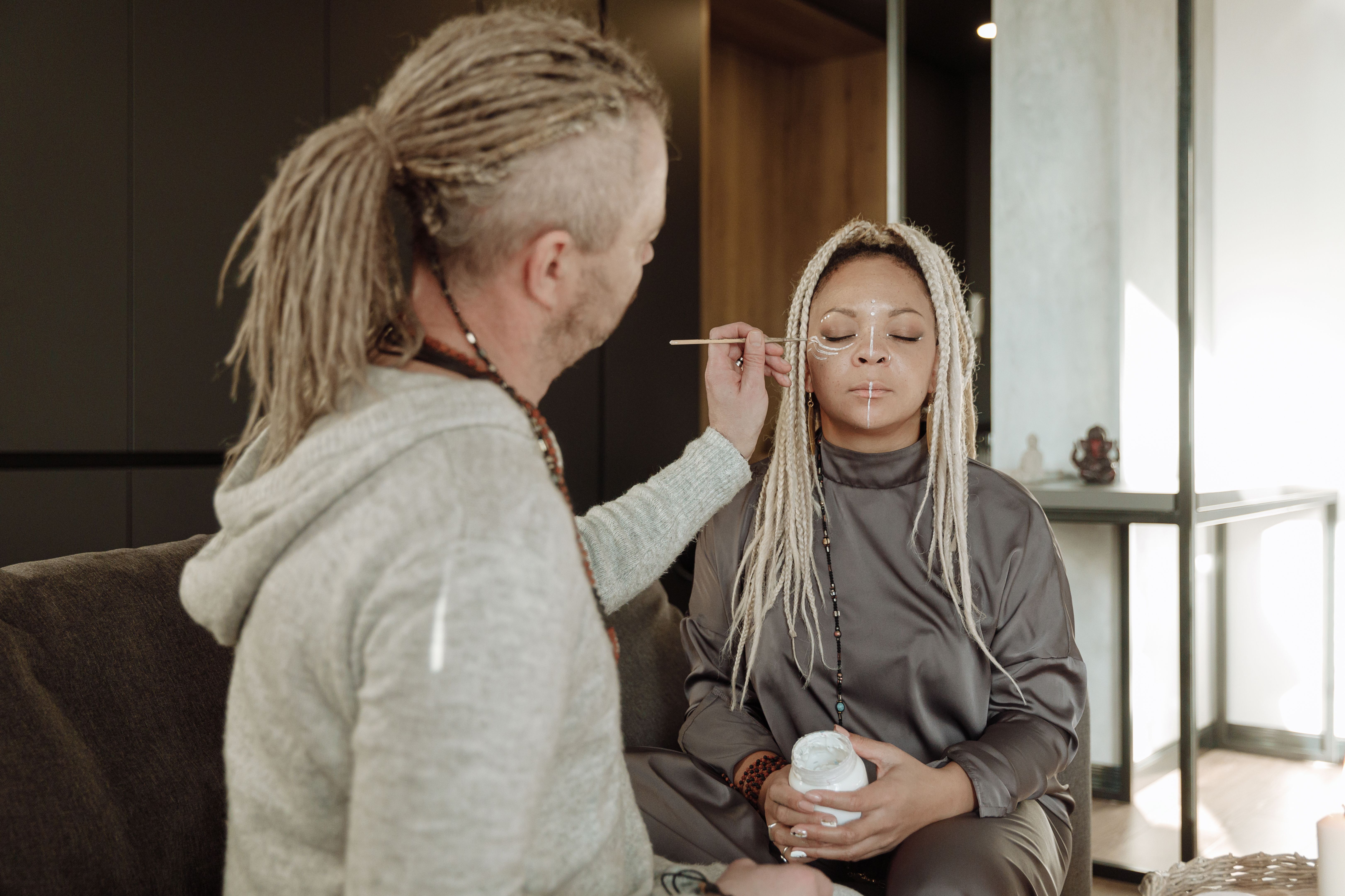 Meditative alternative therapy session with face painting indoors, focusing on spiritual connection.