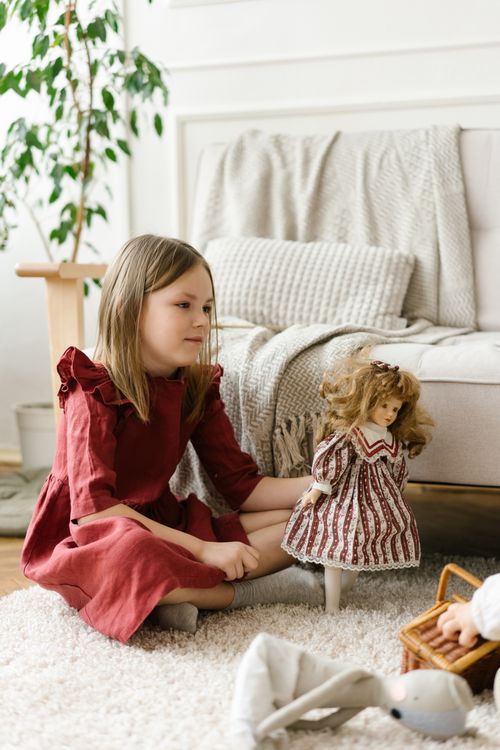 Free Child in red dress playing with dolls on a carpeted floor, indoor setting. Stock Photo
