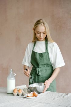 Woman in apron whisking batter in kitchen, preparing homemade baked goods.