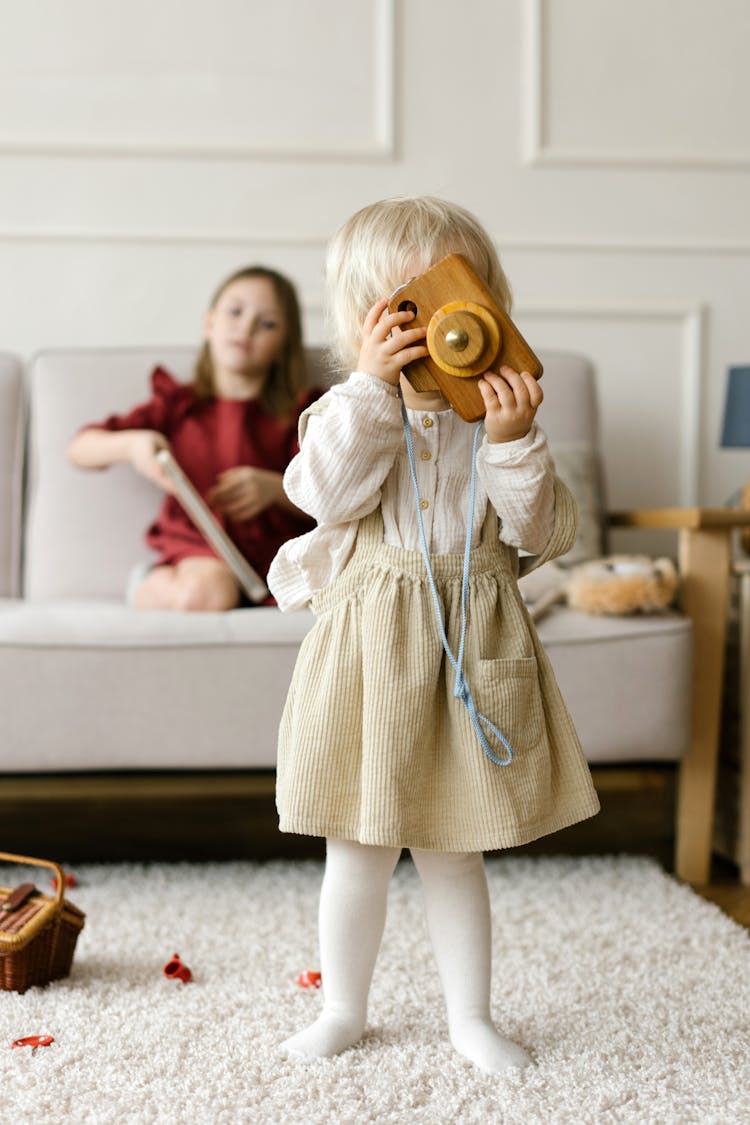 A Kid Holding A Wooden Toy While Standing On A Carpeted Flooring