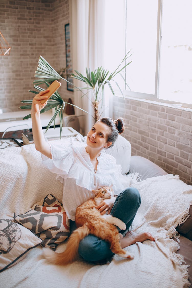 Happy Woman With Cat Taking Selfie On Bed