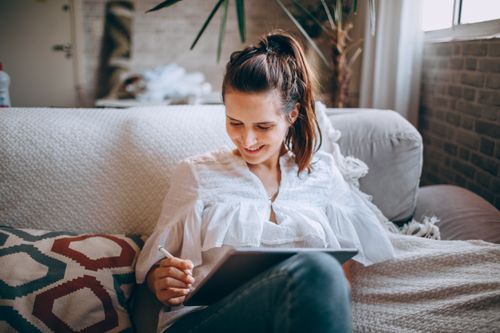 Free Cheerful female in casual clothes sitting on comfortable couch and browsing internet on netbook Stock Photo