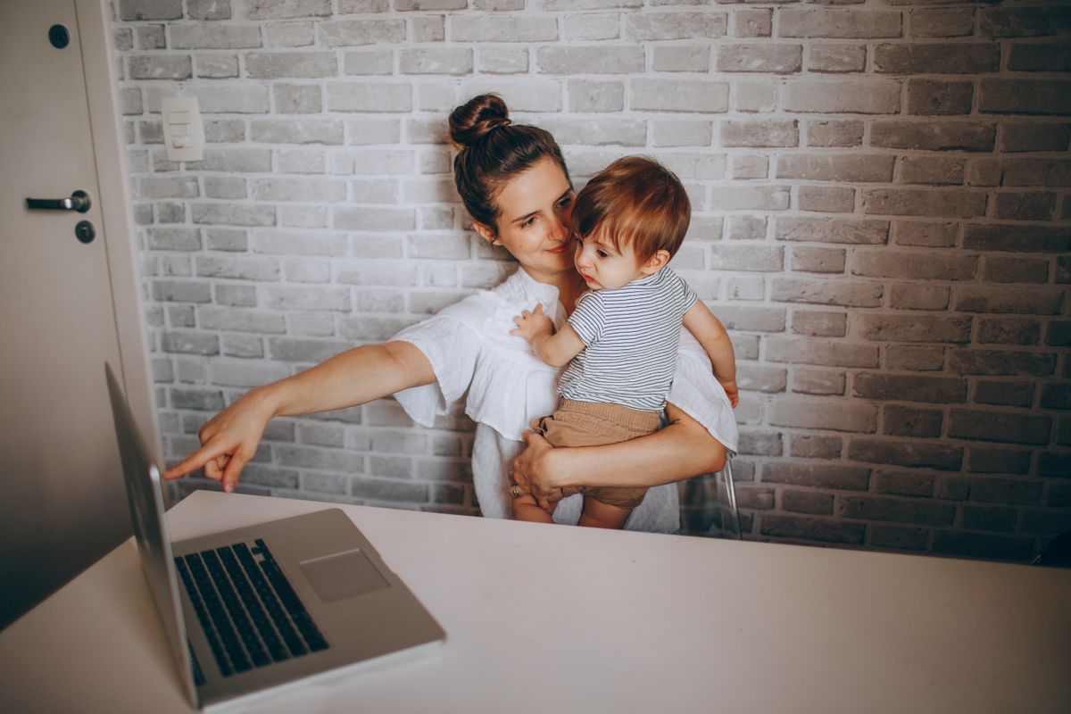 Mother holding her child while using a laptop at home
