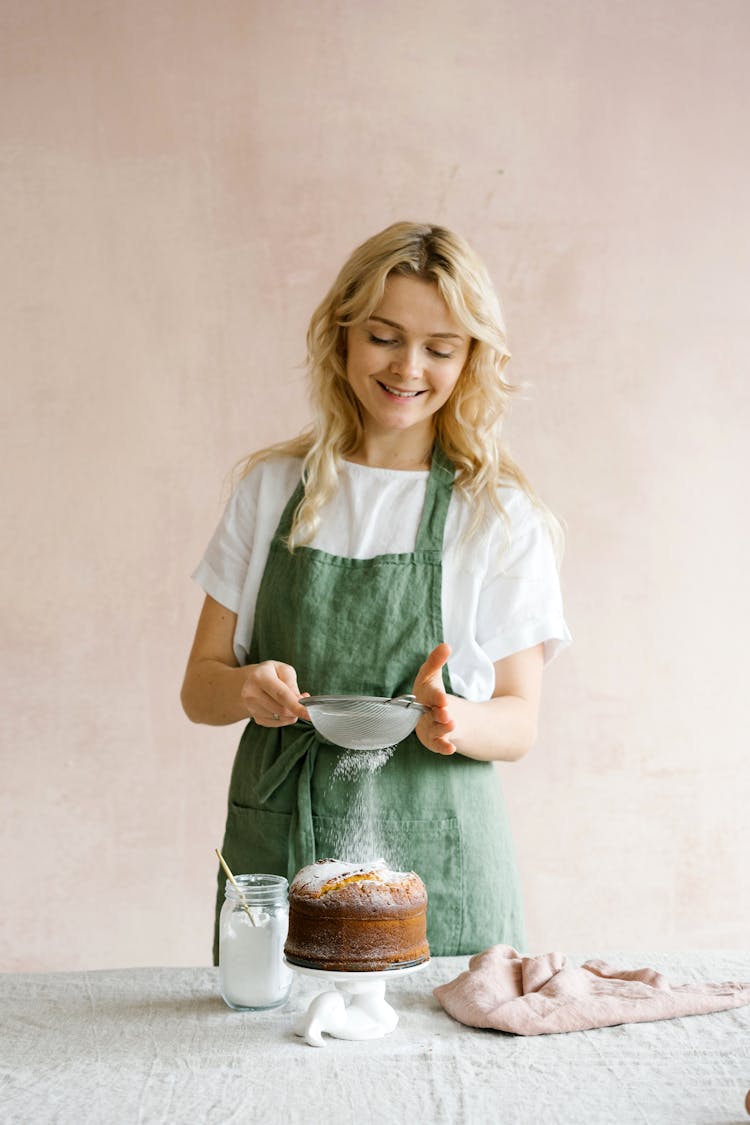 Woman Sprinkling Confectioner's Sugar On Baked Cake