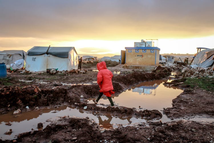 Unrecognizable Girl Walking On Mud Against Poor Houses