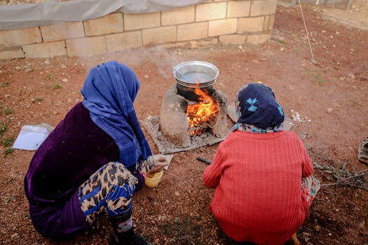 Two women prepare food over an open fire outdoors in Idlib, Syria. Cultural scene of daily life.