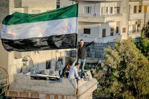 Ethnic men with Syrian flag showing peace gesture on roof