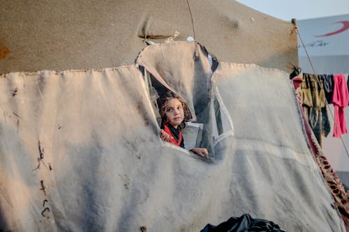 Contemplative ethnic girl peeping out of tent hole