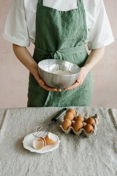 Person in green apron holding stainless steel bowl for baking at home.