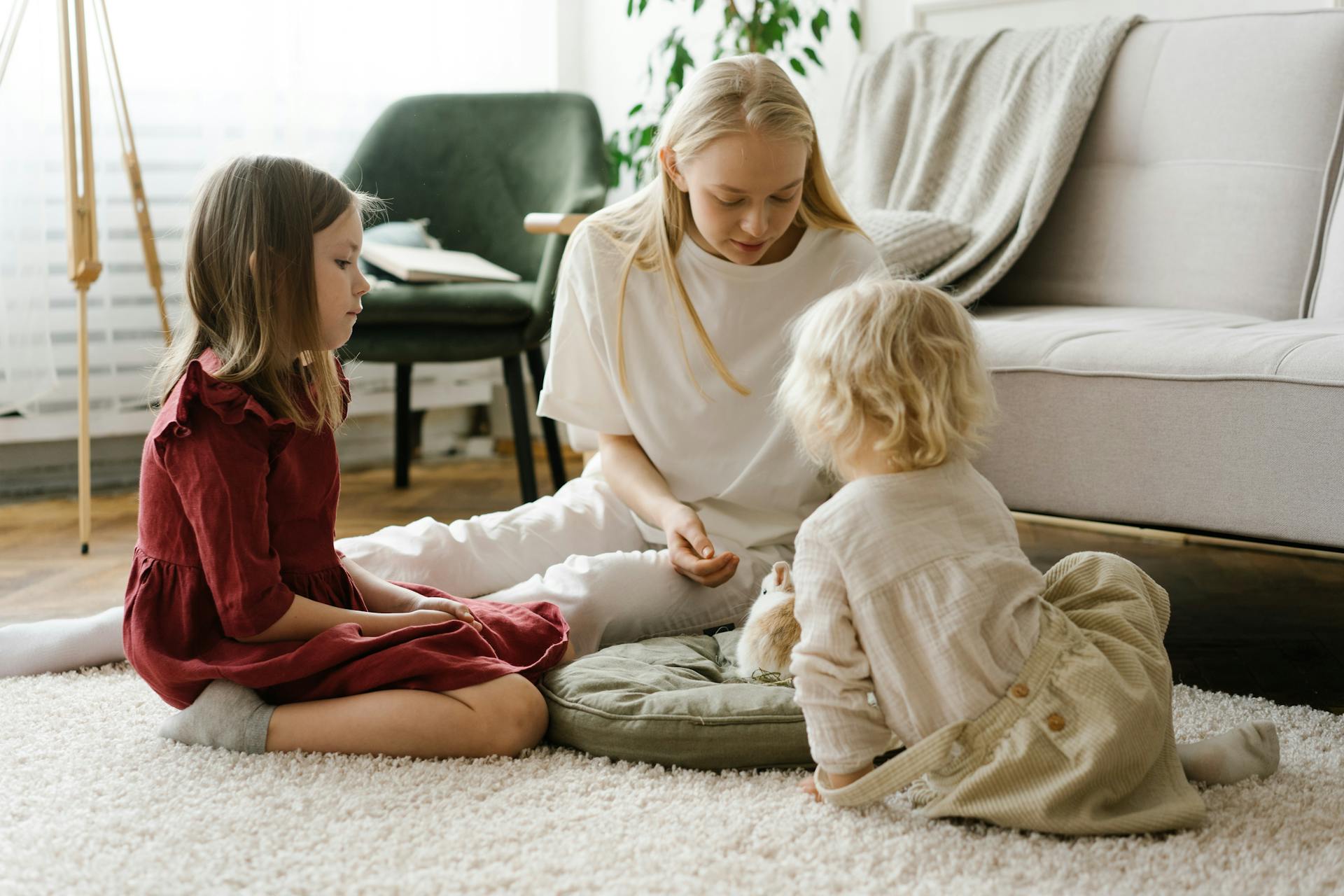 A woman and two children playing together on a cozy indoor carpet, fostering family bonds.