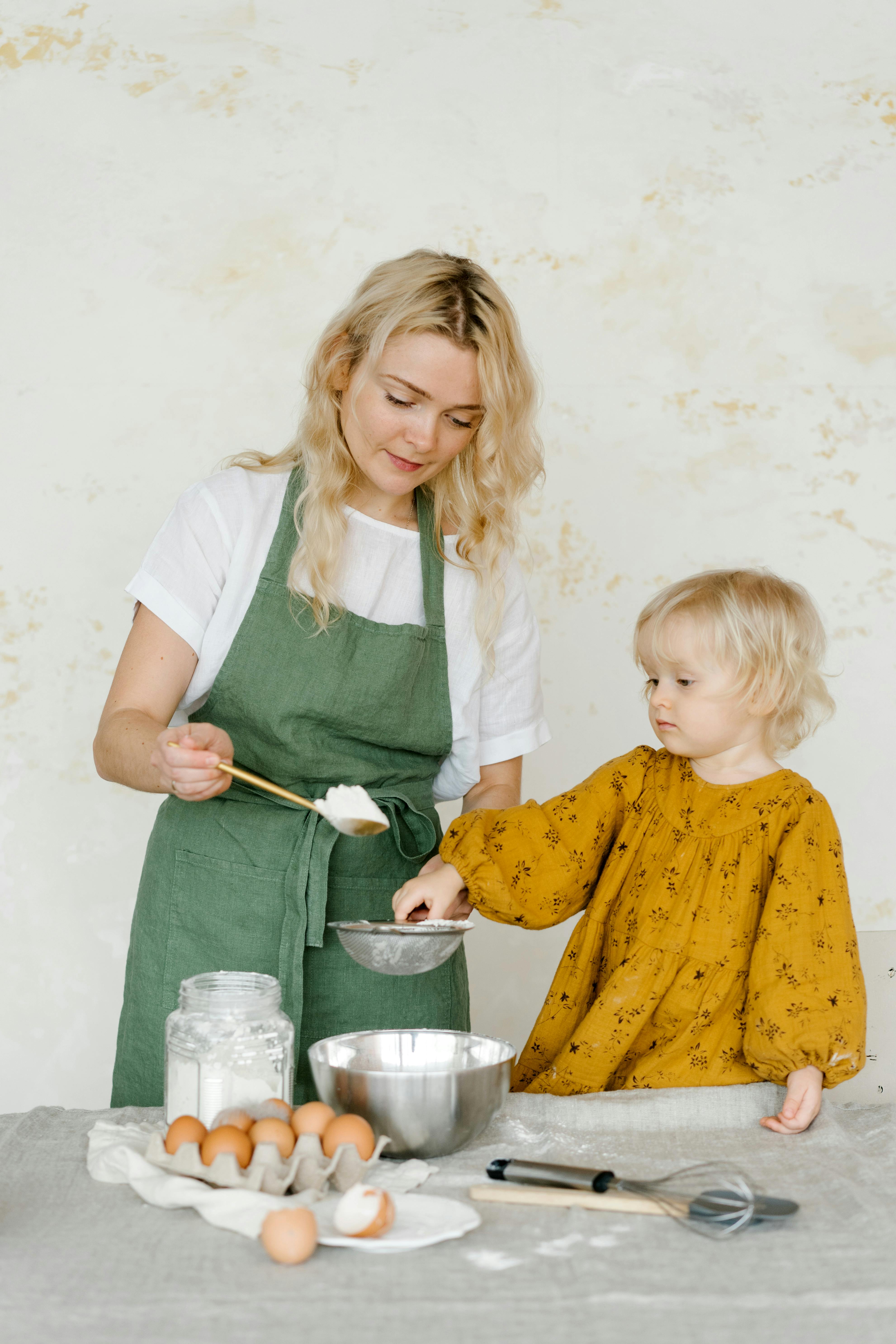 a woman and a girl holding a strainer and a spoonful of flour