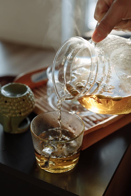 A Person Pouring Tea in Glass Cup