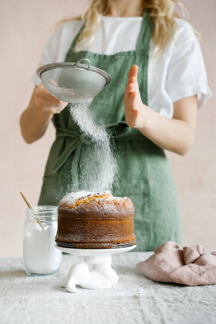 A Woman Sprinkling Powdered Sugar On Top Of The Cake