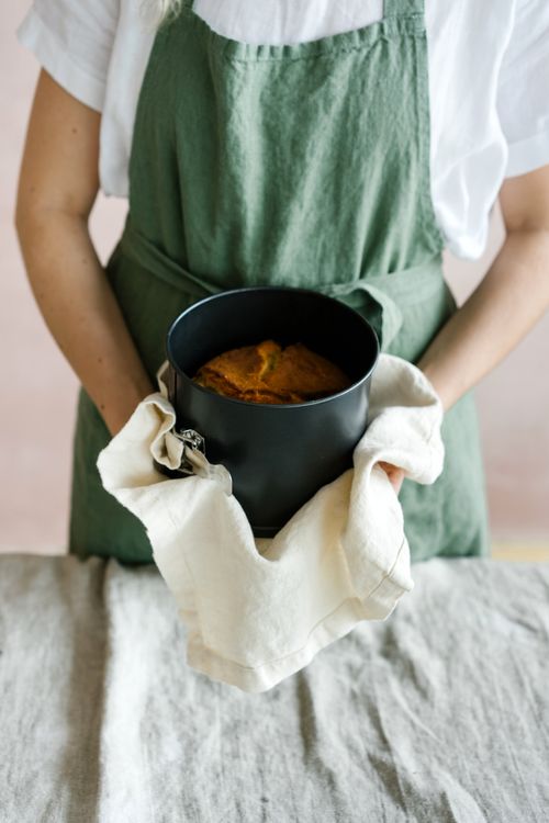 Free A woman wearing a green apron presents a freshly baked cake in a black pan. Stock Photo