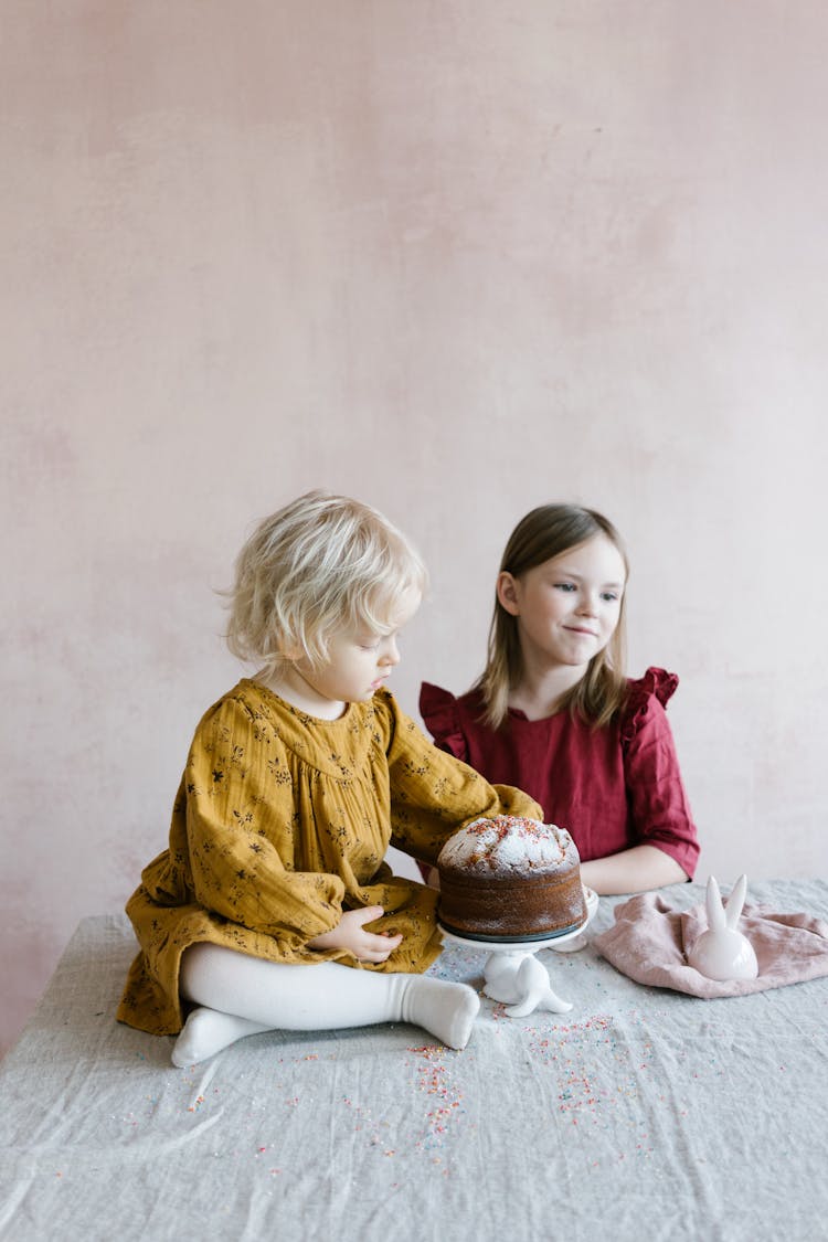 A Girl Beside A Baby Sitting On Table Beside Chocolate Cake