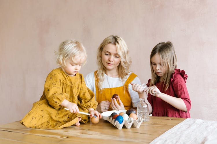 A Young Woman Beside A Baby Sitting On Table Painting An Egg