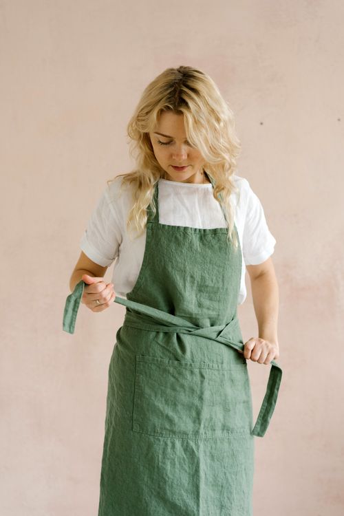 Free A woman in a green apron adjusts it, standing against a neutral background indoors. Stock Photo