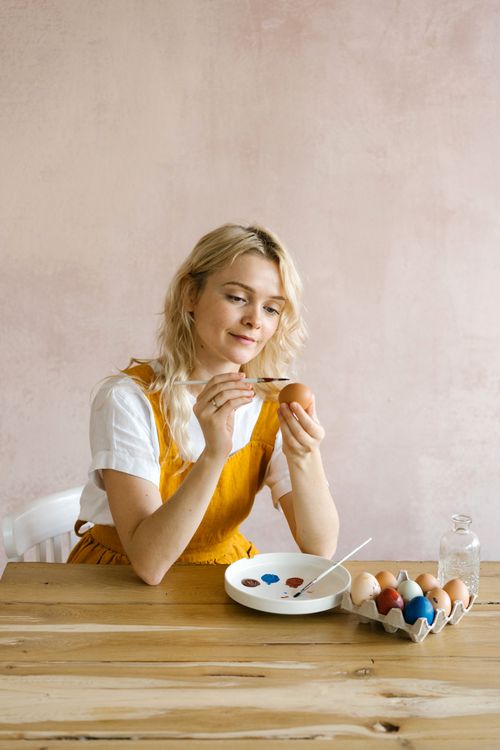 Free Woman painting Easter eggs with colorful paints on a wooden table indoors. Stock Photo