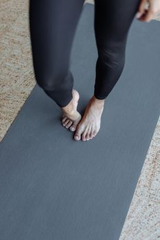 Close-up of a woman's bare feet on a yoga mat, wearing black leggings, indoors.