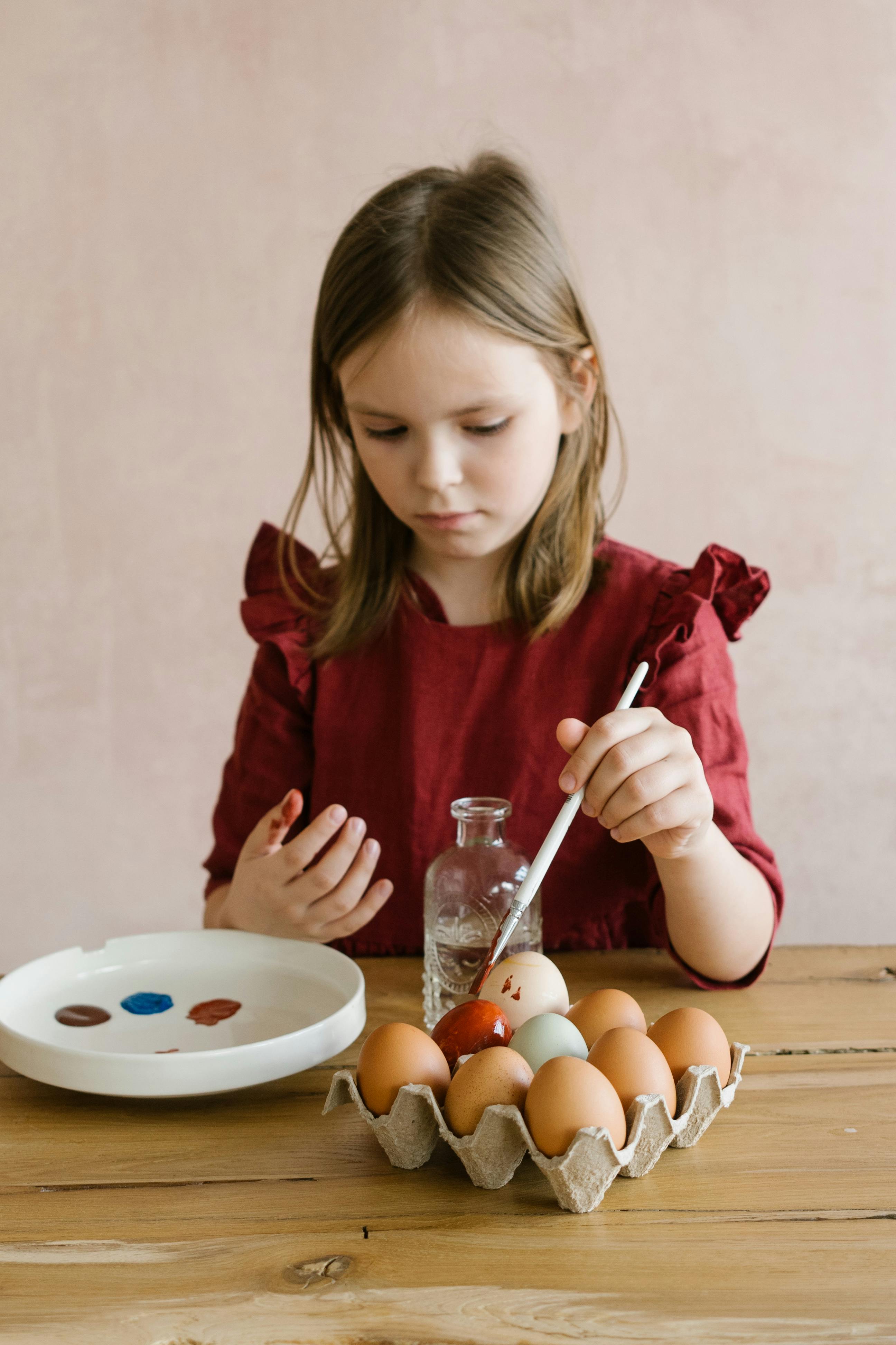 a girl in red long sleeve shirt painting the eggs