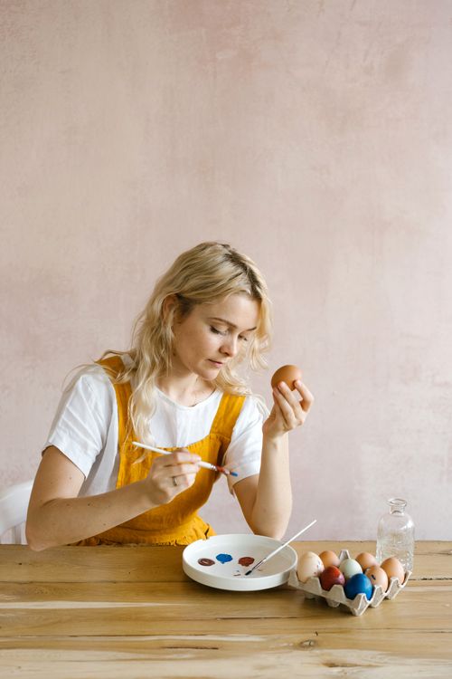 Free A woman decorates Easter eggs with paintbrushes in a creative and artistic DIY setup indoors. Stock Photo
