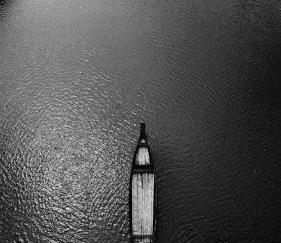 一张黑白航拍照片中，一艘孤船行驶在孟加拉国波光粼粼的河面上