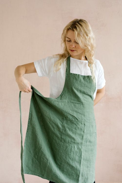 Free Serious female in t shirt putting on apron while preparing for cooking standing against beige wall Stock Photo