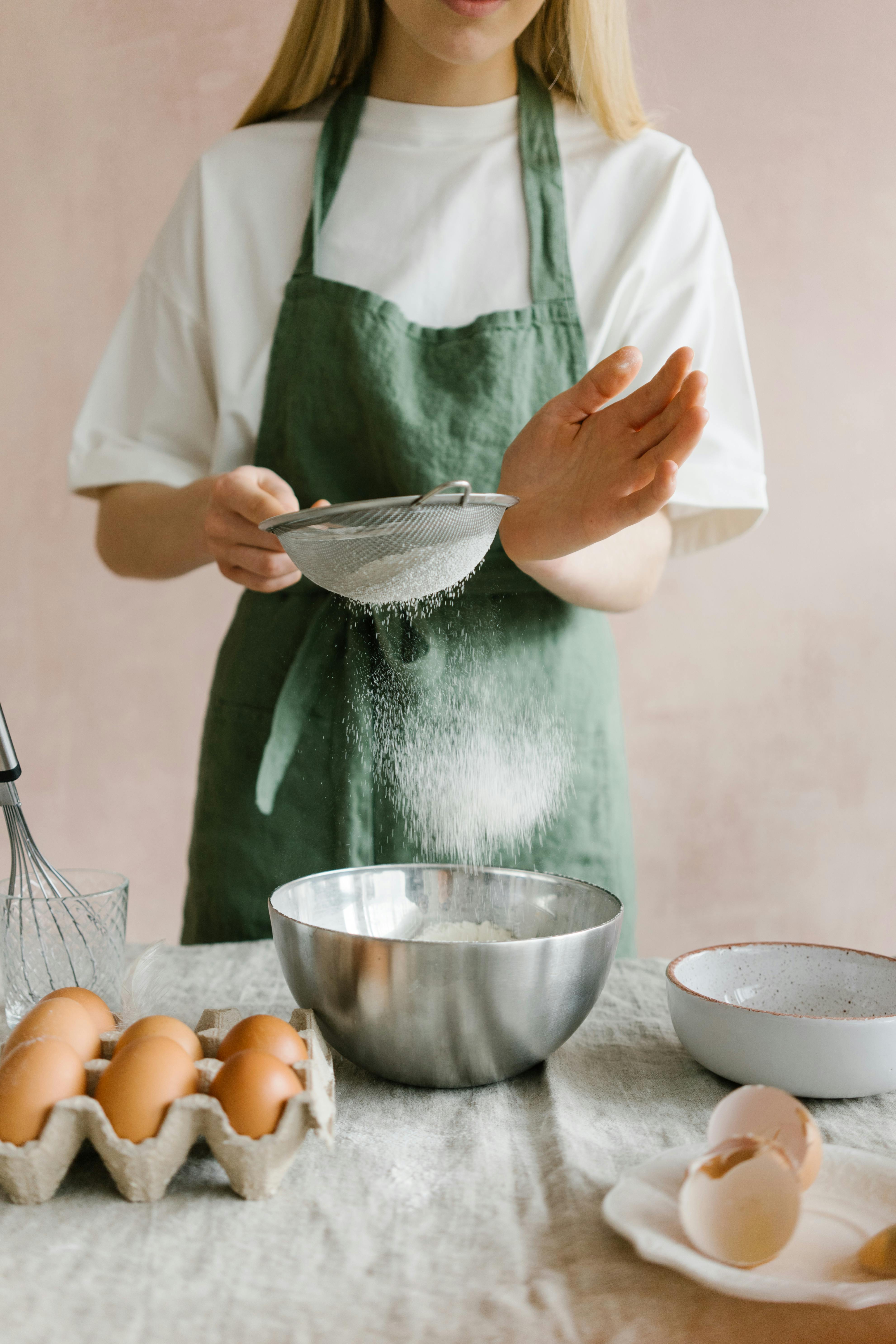 woman sifting flour through sieve at table with eggs