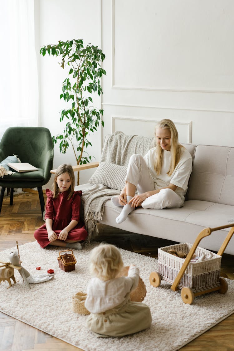 Mother Watching Children Playing With Toys On Soft Carpet