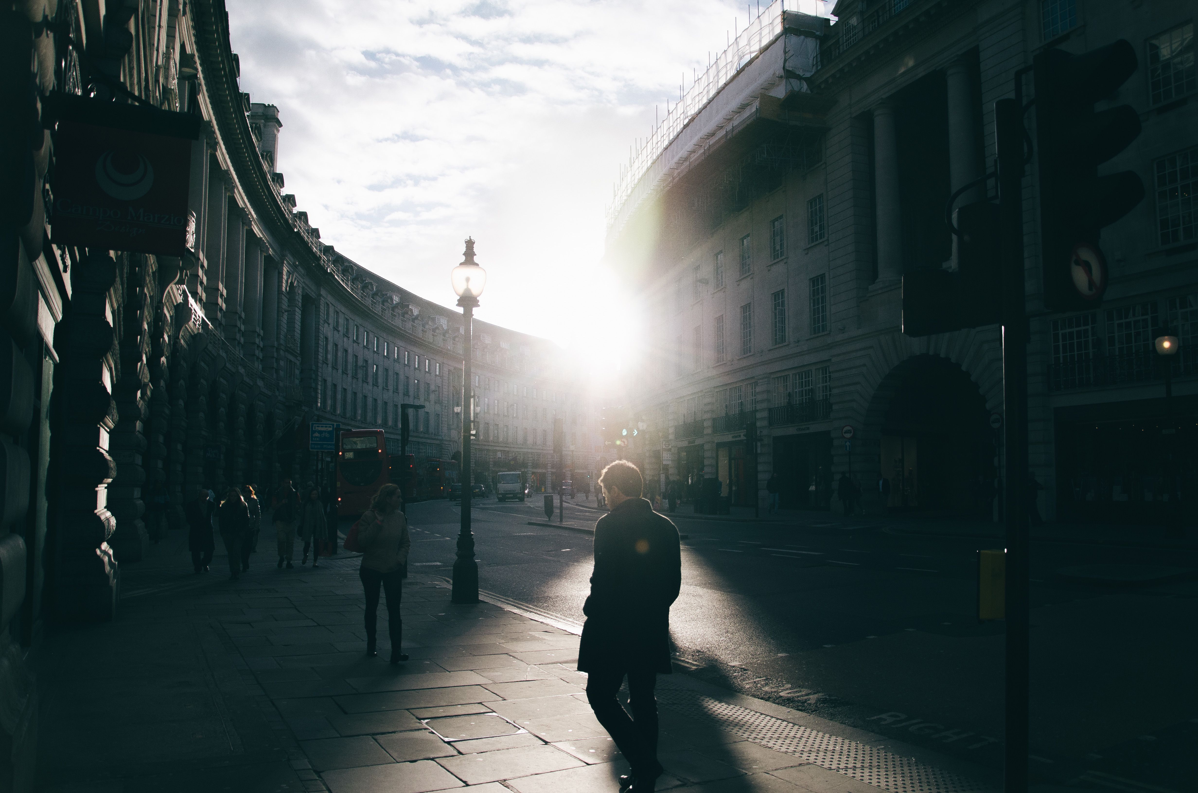 Silhouetted pedestrians in a sunlit city street, creating a dramatic urban scene.