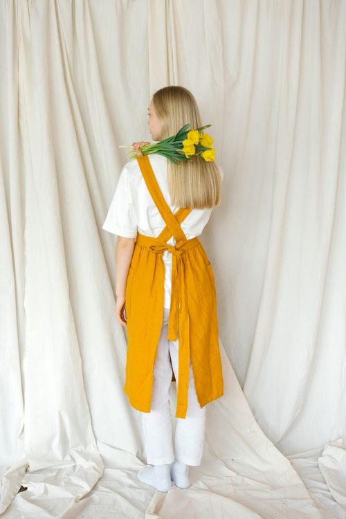 Free Back view of young female with blond hair in casual clothes standing with bouquet of fresh daffodils against light fabric background in studio Stock Photo