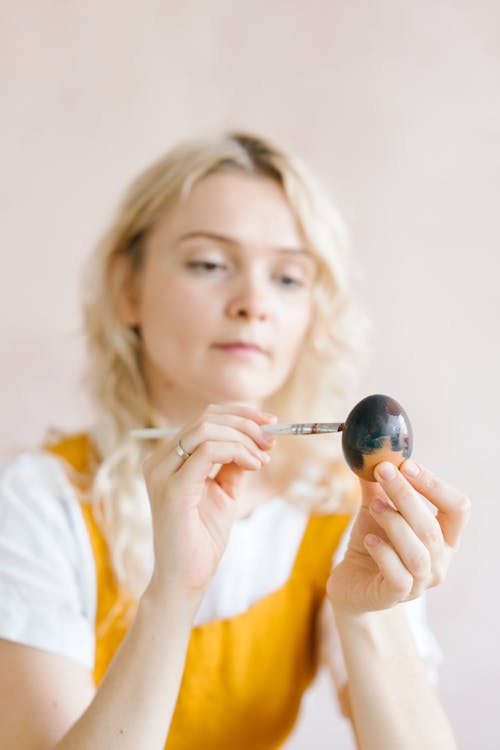 Woman painting egg with brush in studio