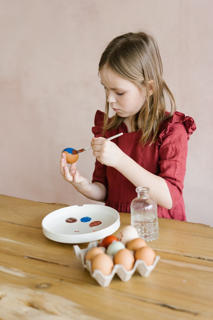 Kid Painting Egg With Brush Near Table With Bottle