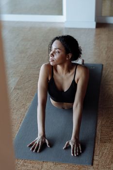 African American woman performing yoga indoors on a mat, focusing on flexibility and relaxation.