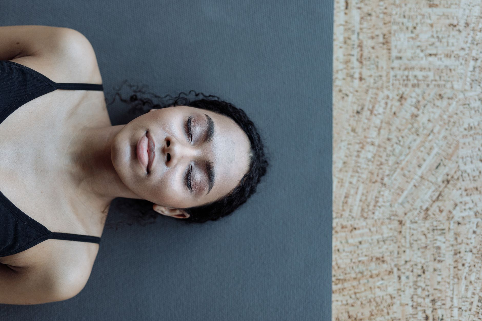 A serene portrait of a woman with curly hair lying on a yoga mat indoors, exuding calmness.