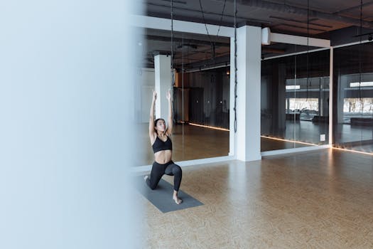 Woman practicing a yoga pose on a grey mat in a modern indoor gym setting.