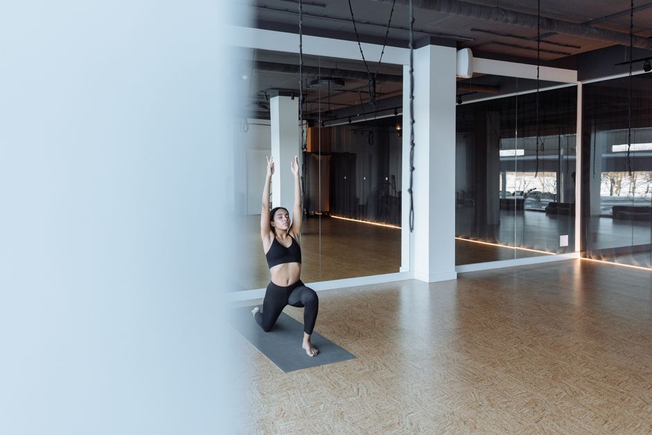 Woman practicing a yoga pose on a grey mat in a modern indoor gym setting.