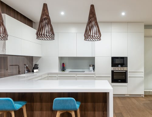 Free Turquoise chairs at counter with white cupboards and modern kitchenware in spacious light kitchen with hanging lamps in contemporary apartment Stock Photo