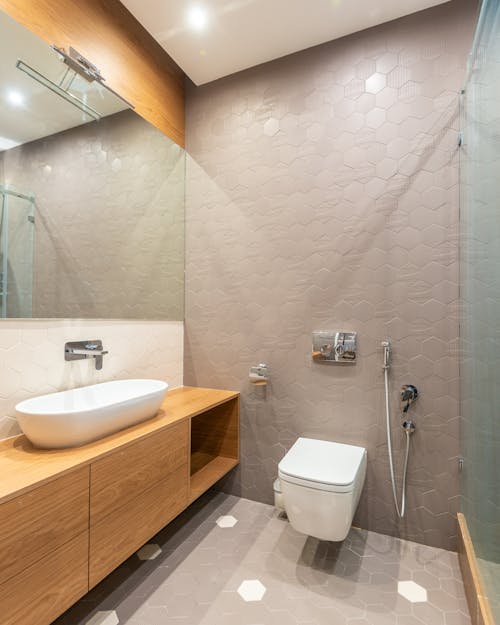 Wooden cabinet with sink with faucet at wall with mirror placed near modern bidet in contemporary spacious bathroom at home