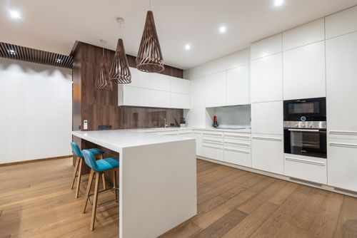 Free Chairs at table near white cupboards and modern kitchenware with oven in spacious stylish kitchen with hanging lamps in contemporary flat Stock Photo