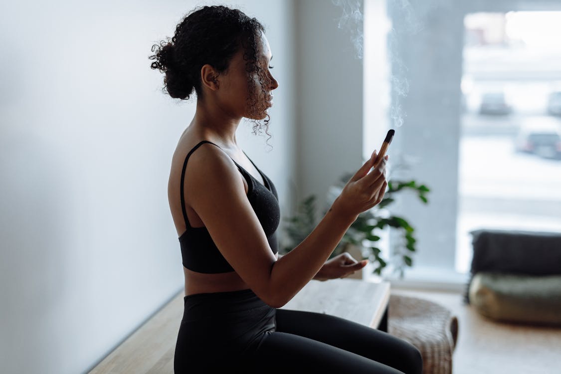 woman in black sports bra holding a burning palo santo 