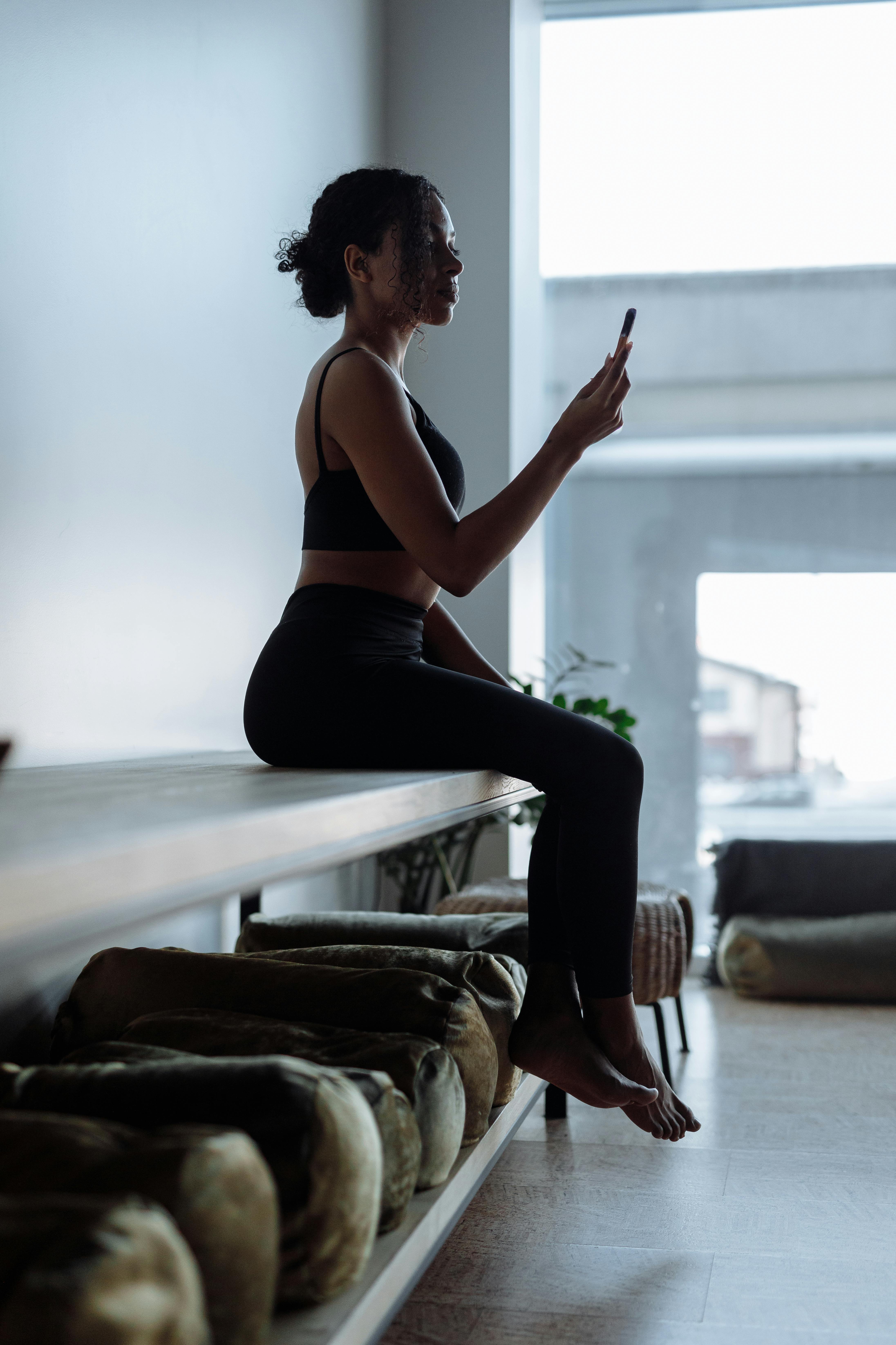 Woman in Black Tank Top and Black Pants Sitting on Bed