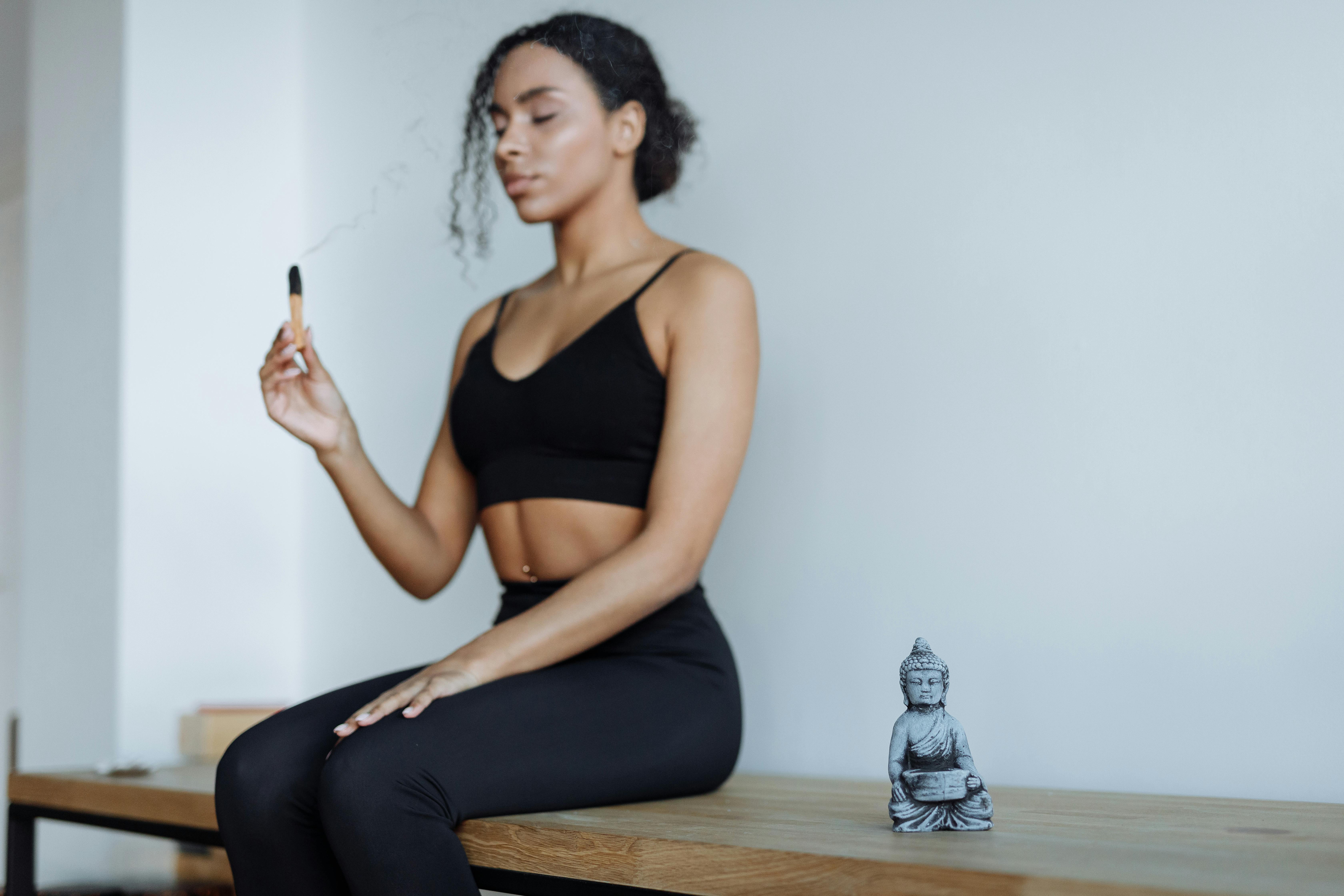 Young woman in meditation holding Palo Santo stick indoors, embracing calm and focus.