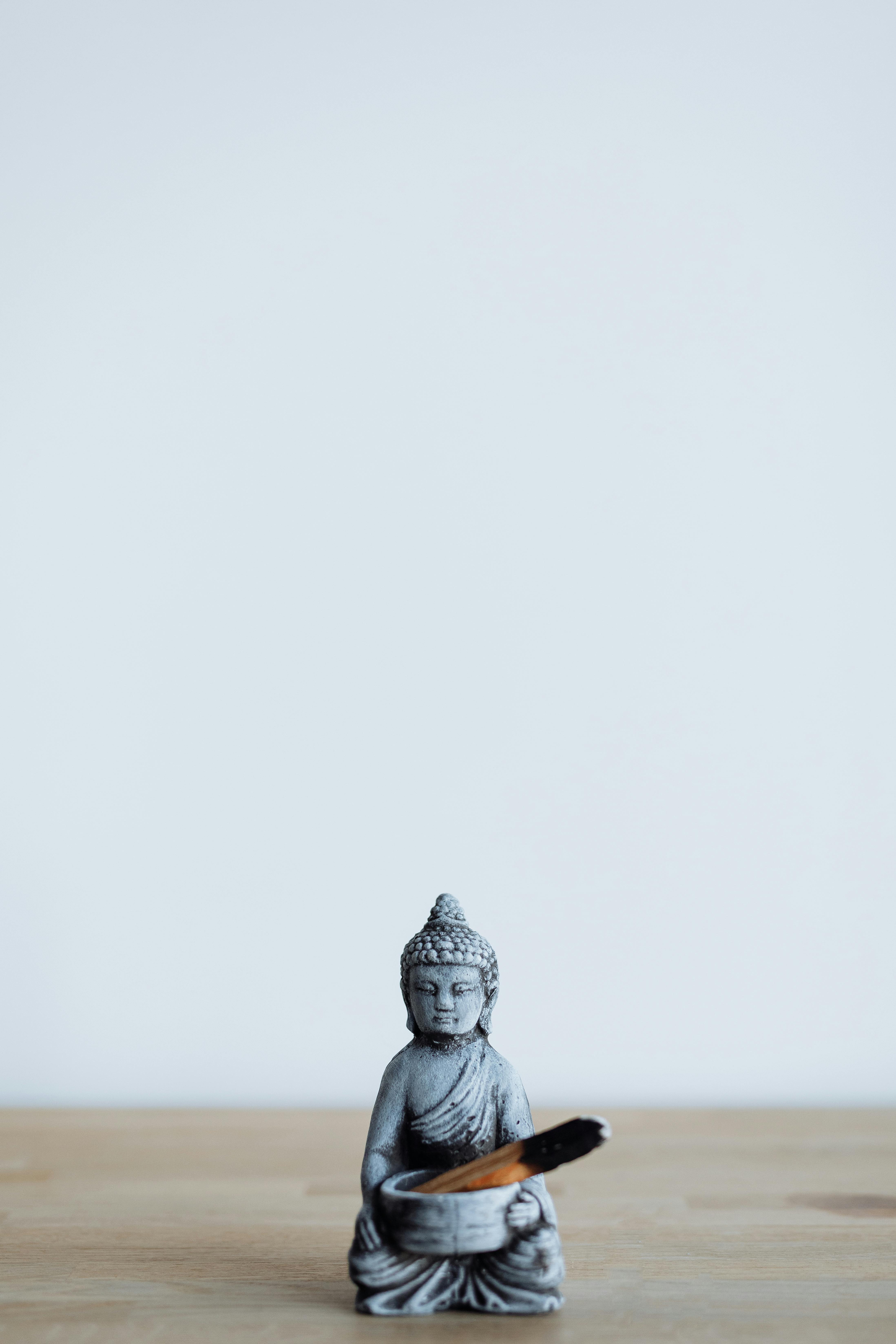 Serene Buddha figurine holding palo santo against a minimalist white background.