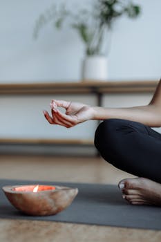 Close-up of a person's hand performing a yoga mudra next to a lit candle, evoking tranquility.