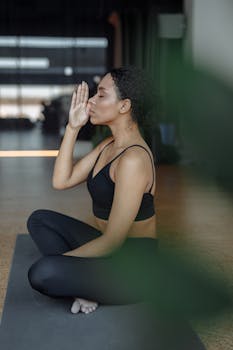 African American woman practicing yoga meditation indoors with eyes closed, creating a serene atmosphere.