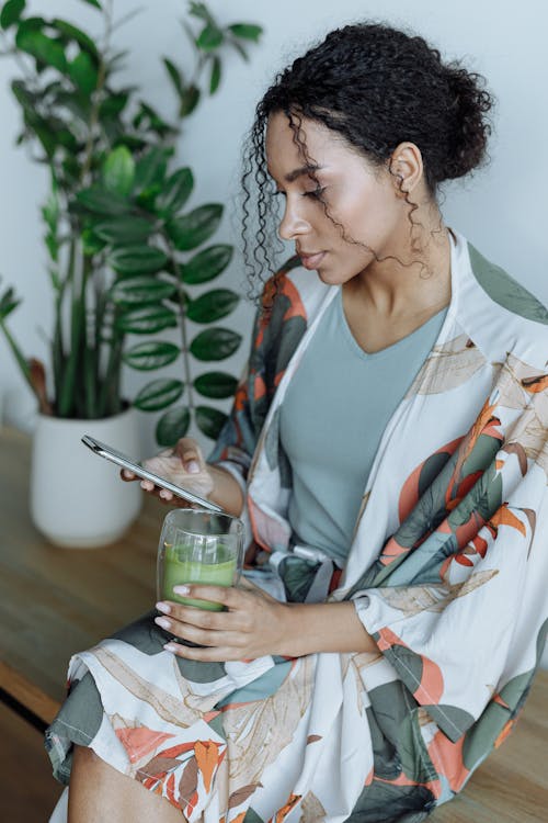 A Woman Using Her Cellphone while Holding a Glass of Matcha Tea