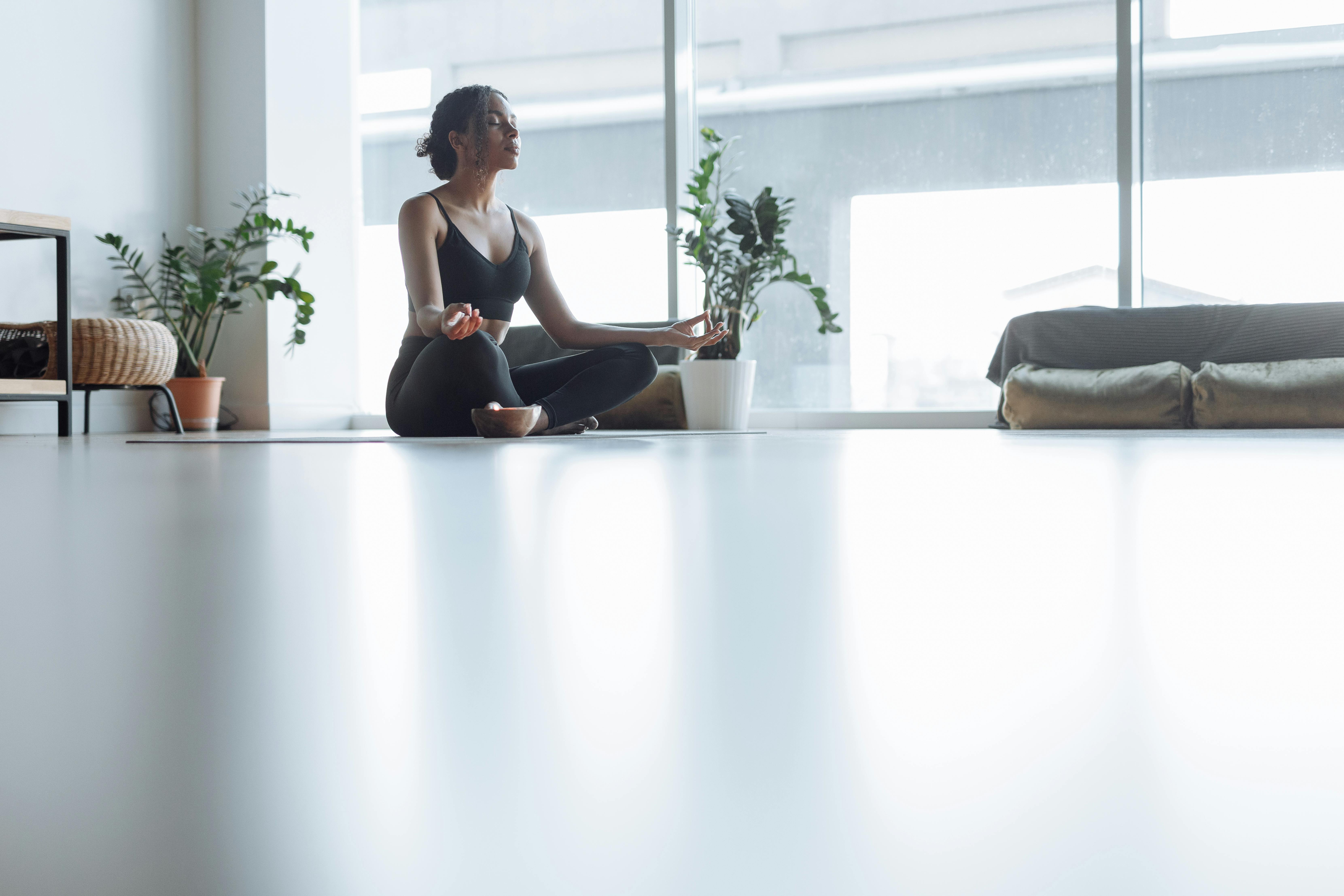 Peaceful adult woman meditating in a modern indoor setting with natural light entering through large windows.