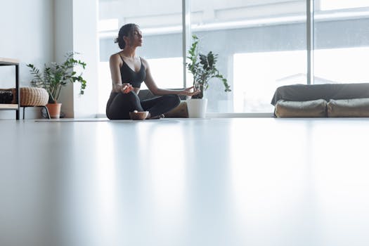 Peaceful adult woman meditating in a modern indoor setting with natural light entering through large windows.