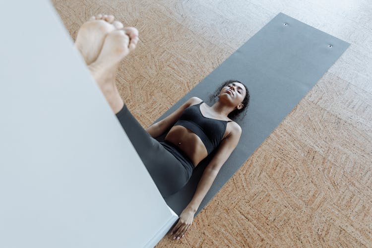 Woman In Black Active Wear Lying On A Yoga Mat While Leaning Her Legs On The Wall